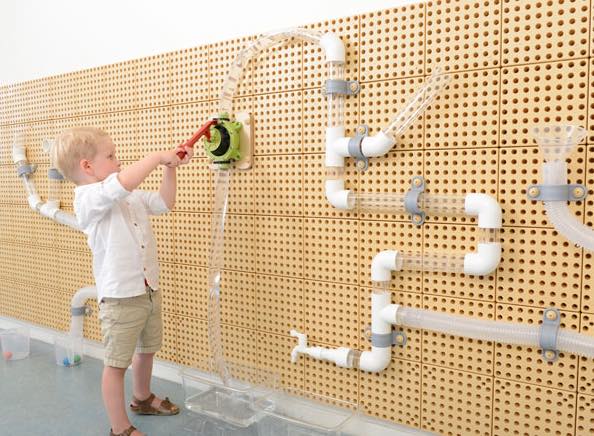 Child playing with a toy on a wall with white pipes and connectors