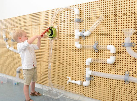 Child playing with a toy on a wall with white pipes and connectors
