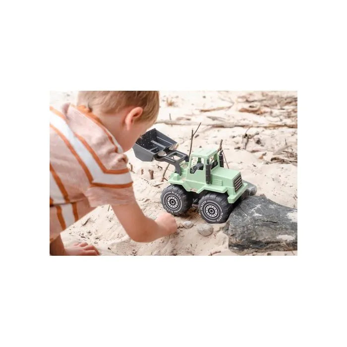 A child in a striped shirt plays with a light green toy dump truck with a black bucket in sand next to a rock.