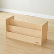A light natural wood three-tier bookshelf or organizer stand on a light wood floor against a white wall.