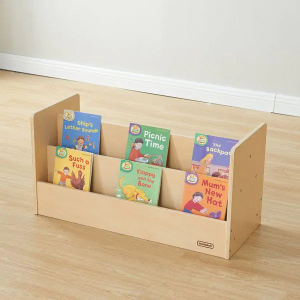 A light natural wood children's book organizer with six front pockets holding colorful children's books, placed on a light wood floor against a white wall.